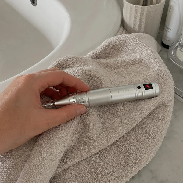 Nærbillede af hånd der holder Feevra Microneedling Dermapen på håndklæde